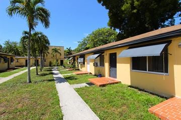 Miami apartment for rent - A yellow building with a black awning is surrounded by green grass and trees.