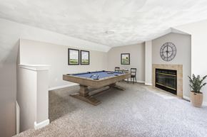 Shirley apartment for rent - A loft space with pool table in a room with a fireplace and a clock on the wall with carpet floor at Birchwood Hills Townhomes in Shirley, MA.