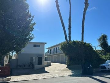 San Diego apartment for rent - A white house with a black door is surrounded by trees and a car is parked in front.