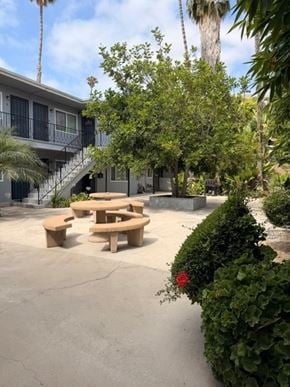 San Diego apartment for rent - A concrete patio with a table and chairs surrounded by greenery and a building in the background.