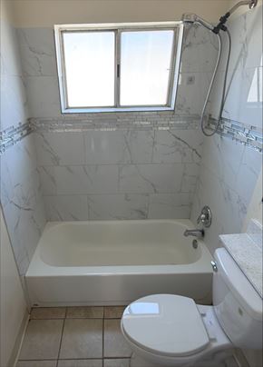 San Diego apartment for rent - A white toilet sits next to a bathtub in a bathroom with marble tile walls.