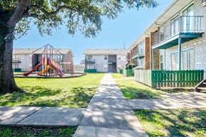 Harvey apartment for rent - A playground with a slide is in the middle of a grassy area between two apartment buildings.