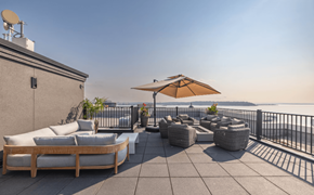 Seattle apartment for rent - A patio with a couch, chairs, and an umbrella overlooking a body of water.