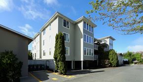 Seattle apartment for rent - A large grey building with a parking lot in front.