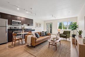 Seattle apartment for rent - Open living room and kitchen with wood floors, leather couch, dining table, dark cabinets, and stainless appliances.
