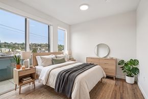 Seattle apartment for rent - Bedroom with a queen bed, two nightstands, a dresser, and oversized windows overlooking the neighborhood.