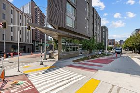 Seattle apartment for rent - A crosswalk with red and white stripes is in front of a building with a glass facade.