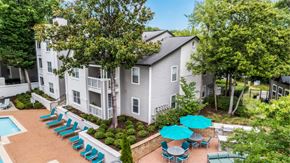 Dunwoody apartment for rent - A pool surrounded by chairs and umbrellas is in front of a building.