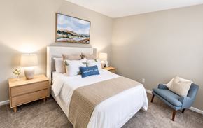Grayson apartment for rent - A bedroom with a large bed, a nightstand with a lamp, a chair, and a painting on the wall.