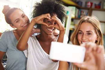Three friends are making a heart shape with their hands while taking a selfie.