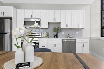 Hartford apartment for rent - A kitchen with white cabinets and a wooden table with two vases on it.