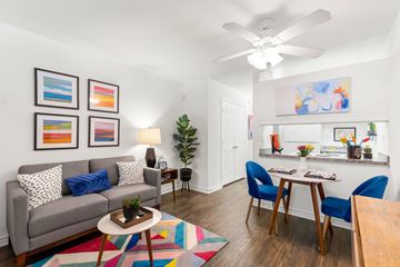 Metairie apartment for rent - A living room with a grey couch, a coffee table, a dining table with chairs, a ceiling fan, and a painting on the wall.