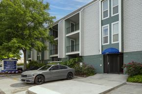 Metairie apartment for rent - A grey car is parked in front of a building with a blue sign that says "Tonini".