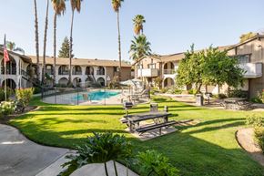 Visalia apartment for rent - A pool surrounded by a fence and a bench in the foreground.
