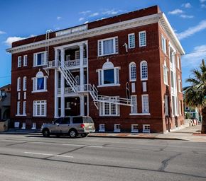 El Paso apartment for rent - A red brick building with a white balcony and a silver minivan parked in front.