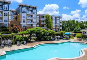 Cary apartment for rent - A swimming pool surrounded by lounge chairs and trees in front of apartment buildings.