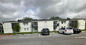 Gretna apartment for rent - A parking lot in front of a white apartment building with cars parked.