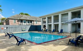 Terrytown apartment for rent - A pool surrounded by chairs and an umbrella in front of a building.