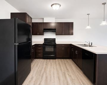 Monaca apartment for rent - A black refrigerator stands in a kitchen with wooden floors and brown cabinets.