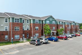 Muscatine apartment for rent - A parking lot with cars and apartment buildings in the background.