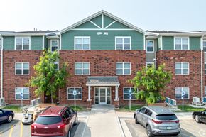 Muscatine apartment for rent - A red car is parked in front of a brick building with a green awning.