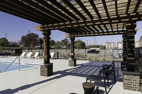 Dallas apartment for rent - A wooden pergola over a pool with lounge chairs underneath.