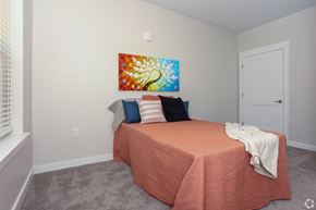Palestine apartment for rent - A bedroom with a bed covered in a peach sheet and a colorful painting on the wall.