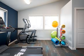 Post Falls apartment for rent - Fitness center with white walls and one dark blue accent wall. An elliptical machine, treadmill and stand with exercise balls and yoga mats are visible.at North Pointe, Post Falls