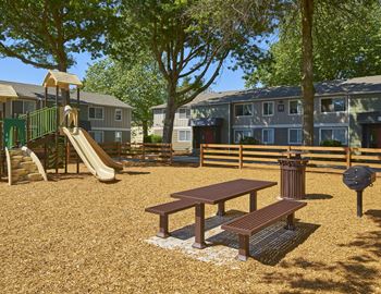 A playground with a slide and a picnic table in front of apartments