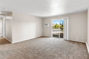 Post Falls apartment for rent - Spacious living room with sliding glass doors, tree-lined views, and plush carpeting at The Overlook at Falls Park Apartments.