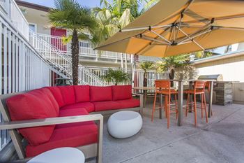 A patio with a red couch and a table with chairs and umbrellas 