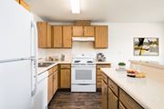 Post Falls apartment for rent - A kitchen with hardwood floors, top and bottom cabinet storage, and white appliances. Breakfast bar and island to the right.at Clearwater, Post Falls, 83854
