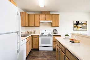 Post Falls apartment for rent - A kitchen with hardwood floors, top and bottom cabinet storage, and white appliances. Breakfast bar and island to the right.at Clearwater, Post Falls, 83854