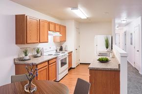 Lewiston apartment for rent - Bright kitchen with honey-colored cabinets and white appliances and faux wood flooring. You can also see down the hallway with white walls and taupe carpet.at Canyon View, Lewiston