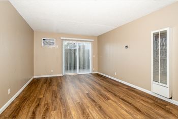The spacious living room of an apartment with wood flooring and sliding glass doors