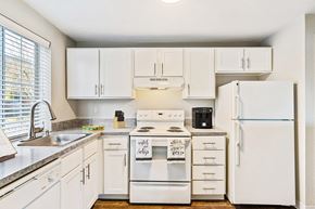 Olympia apartment for rent - L-shaped kitchen with white cabinets, a large window above the sink, and a white dishwasher, oven, stovetop, full-size fridge.at Capitol Crossing, Olympia, WA