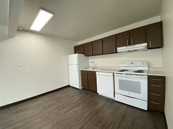 An empty kitchen with white appliances and wood flooring in an apartment