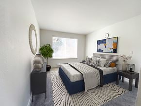 Snohomish apartment for rent - An apartment bedroom with white walls, a large window on the back wall and gray carpet. Staged with a queen-size bed, side tables, a dresser and a rug.at The Trail, Snohomish Washington