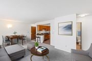 Billings apartment for rent - A living room with a grey sofa, a coffee table, a dining table with chairs, a kitchen area with a sink and a fridge, and a painting on the wall.