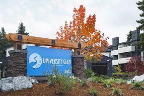 University Place apartment for rent - Community entrance with blue 'University Glen' sign surrounded by green plants, bushes, large rocks, and trees at University Glen, University Place, WA
