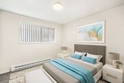 Kennewick apartment for rent - Spacious bedroom with white walls, taupe carpets, and a large window with white blinds. Staged with a bed, side tables, a bench, and art.at Wildflower, Washington, 99336