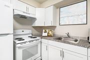 Kennewick apartment for rent - Corner of a kitchen with custom white cabinets, spacious countertops, a stainless steel sink, oven, stovetop and hood range, and full-size fridge.at Wildflower, Washington