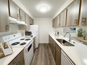 Snohomish apartment for rent - A galley-style kitchen with wood-like flooring, top and bottom cabinet storage, and white appliances. An oven and range, full-size fridge, dishwasher and sink.at The Trail, Snohomish, WA 98290
