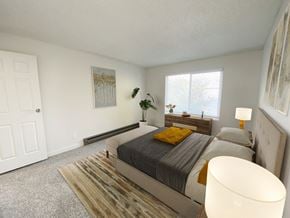 Twin Falls apartment for rent - Bedroom with white walls, oversized window with natural light, gray carpet, staged with bed, side tables, dresser, and plant.at Laurel Park, Twin Falls, 83301