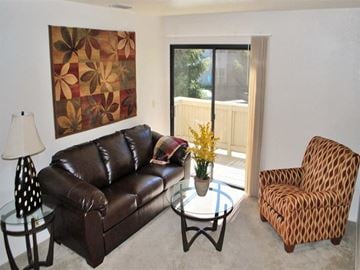 Ranch Cordova apartment for rent - A brown leather couch sits in a living room with a brown patterned chair and a glass coffee table.