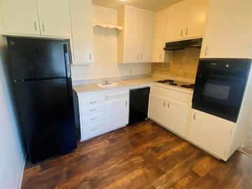 Sacramento apartment for rent - A black refrigerator stands in a kitchen with white cabinets and wooden floors.