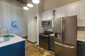 Denver apartment for rent - Industrial Style Apartment with Exposed Concrete and Ducts, Kitchen with Breakfast Bar, White Upper Cabinets and Dark Blue Lower Cabinets Around Stainless Steel Appliances Next to Built in Shelves