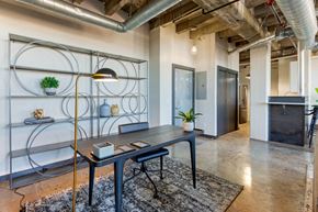 Denver apartment for rent - Industrial Style Apartment  with Exposed Ducts and Concrete, Area Rug Under Desk in Front of Contemporary Shelf with Plants and Decorations Next to Kitchen with Breakfast Bar