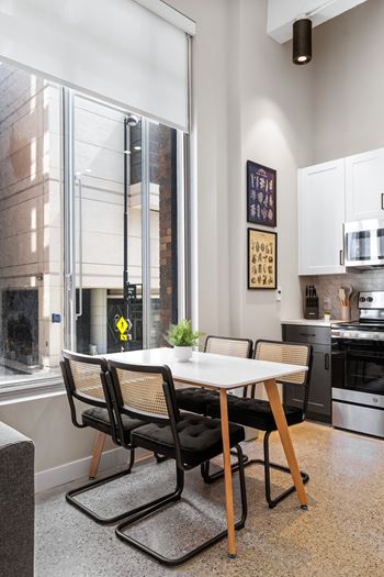 A dining room with a large window and a table with black chairs