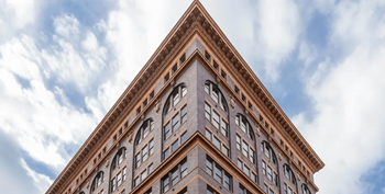 A tall brown building with many windows and a triangular top.
